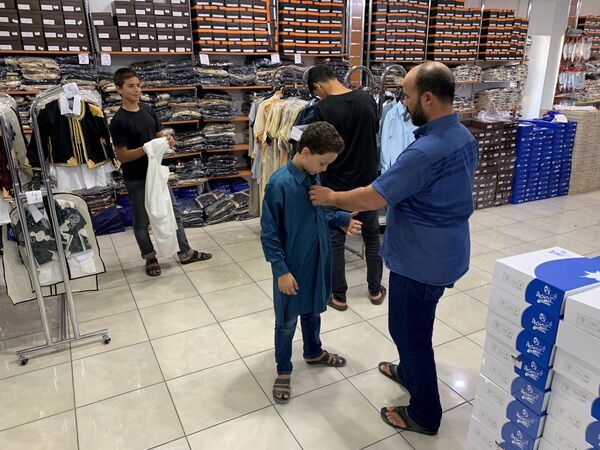 Мужчина примеряет своему сыну одежду в магазине перед празднованием Курбан-байрам в ливийском городе Мисрат - Sputnik Azərbaycan
