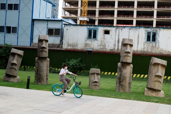 Девушка на велосипеде перед копиями Моаи в деловом районе Пекина  - Sputnik Азербайджан