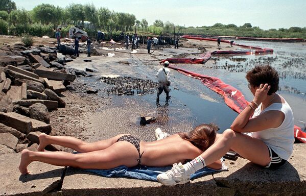 Отдыхающие рядом с рабочими во время очистки пляжа от нефти в Аргентине, 1999 год  - Sputnik Азербайджан