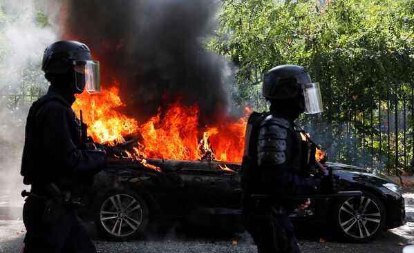 Французские полицейские идут мимо горящей машины во время демонстрации движения желтых жилетов в Париже - Sputnik Azərbaycan