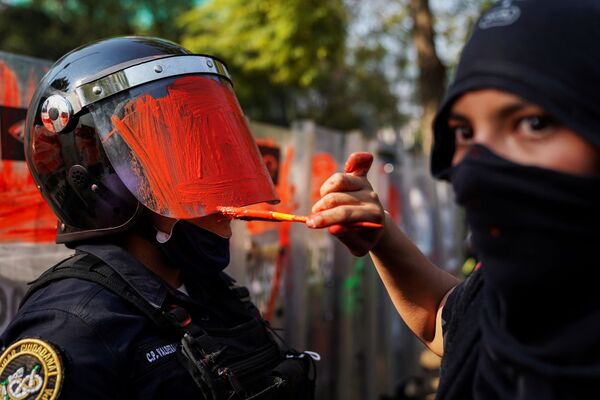 Девушка красит шлем сотрудника полиции во время акции протеста против гендерного и полицейского насилия в Мехико - Sputnik Азербайджан