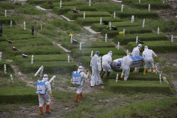 Рабочие в защитных костюмах несут гроб с телом человека, предположительно умершего от коронавируса, к захоронению в Медане, Индонезия - Sputnik Азербайджан