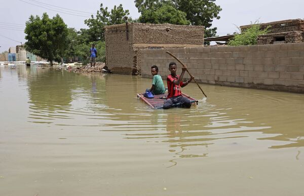 Подростки плывут на плоту по затопленной в результате наводнения улице в городе Салмания, Судан - Sputnik Азербайджан