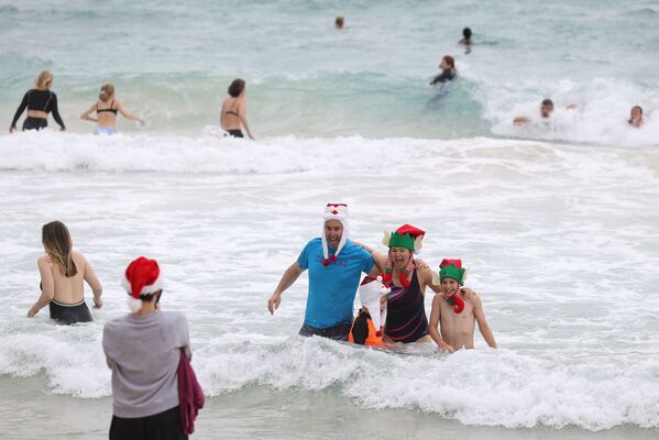 Люди в рождественской одежде позируют для фотографий в Рождество на пляже Бонди в Сиднее, Австралия - Sputnik Азербайджан