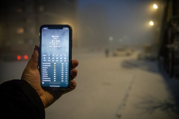 Мужчина демонстрирует мобильный телефон с информацией о прогнозе погоды в Якутске - Sputnik Азербайджан
