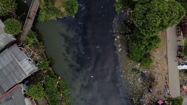 Люди ловят рыбу с деревянного моста на реке Писанг-Бату, протекающей через густонаселенный район и загрязненной бытовыми отходами, в Бекаси, на окраине Джакарты, Индонезия - Sputnik Азербайджан