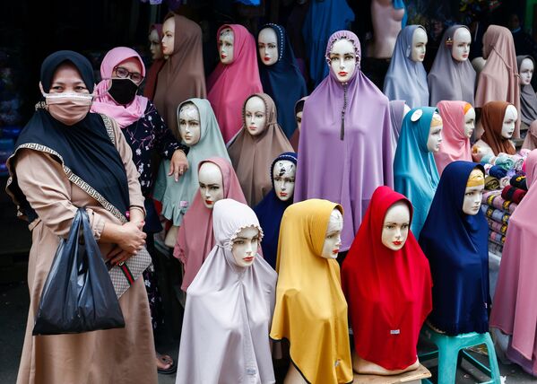 Женщины в защитных масках стоят рядом с хиджабами, выставленными на продажу на текстильном рынке Танах Абанг в Джакарте, Индонезия - Sputnik Азербайджан