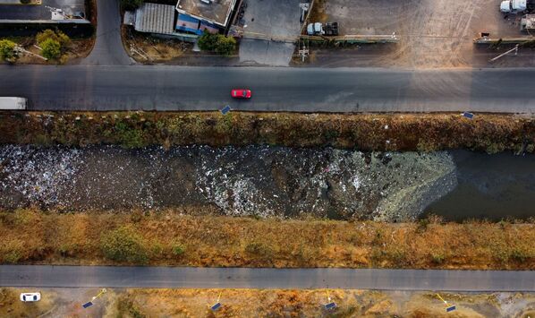 Автомобили, движущиеся рядом с каналом Interceptor Poniente, сильно загрязненном сточными водами и мусором,в Куаутитлане, Мексика - Sputnik Азербайджан
