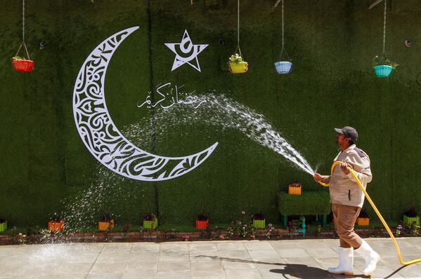 Рабочий распыляет воду рядом с полумесяцем в преддверии священного месяца Рамадан в Наджафе, Ирак - Sputnik Азербайджан