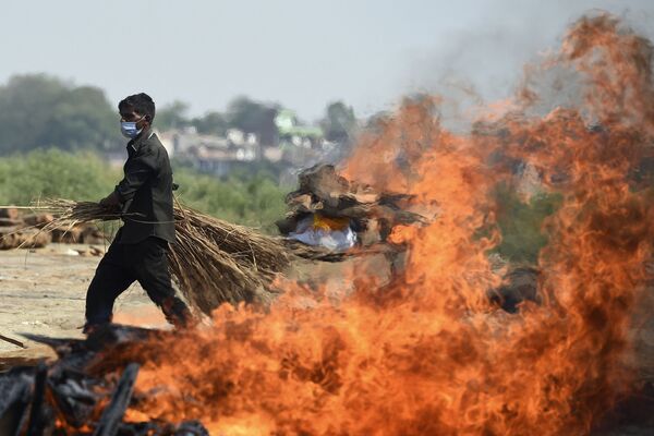 Рабочий проходит мимо горящего погребального костра человека, умершего из-за коронавируса Covid-19, Индия  - Sputnik Азербайджан