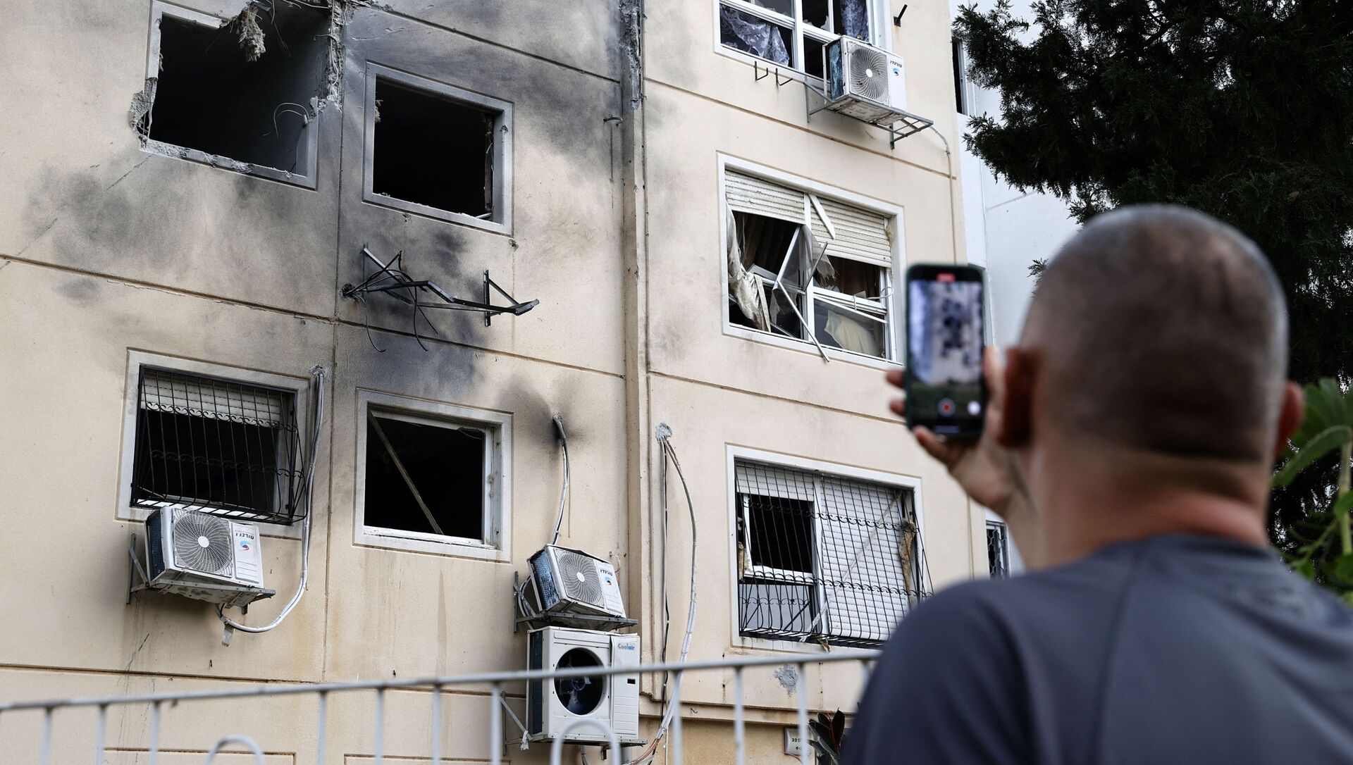 Израильтянин фотографирует поврежденный фасад здания в городе Ашкелон на юге Израиля, 11 мая 2021 года  - Sputnik Азербайджан, 1920, 19.05.2021