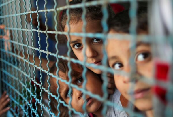 Палестинские дети, покинувшие свои дома из-за израильских воздушных и артиллерийских ударов, смотрят через оконное ограждение школы, управляемой Организацией Объединенных Наций, в которой они укрываются, в городе Газа  - Sputnik Азербайджан
