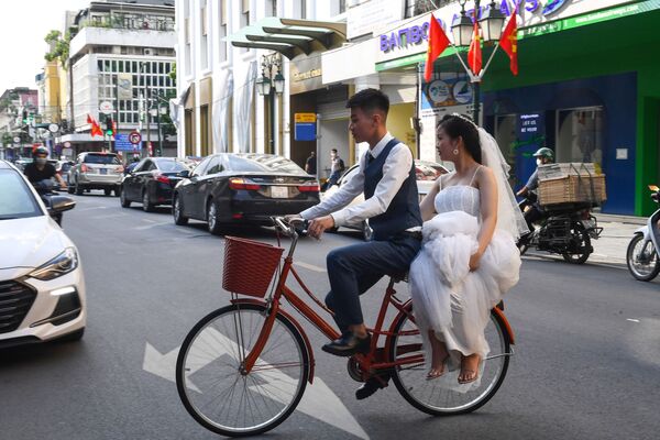 A groom ferries his bride on a bicycle as they pose for wedding photographs on a street in Hanoi  - Sputnik Azərbaycan