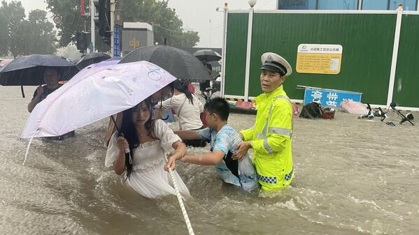 Сотрудник дорожной полиции помогает жителям переходить затопленную дорогу в Чжэнчжоу, Китай  - Sputnik Azərbaycan