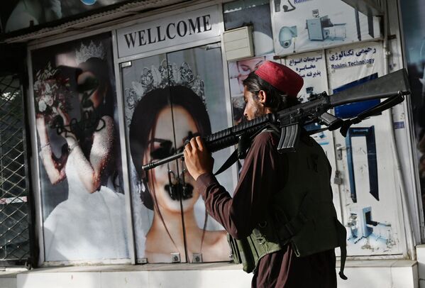 Боевик Талибана ( Террористическая организация, запрещенная в России) у салона красоты с изображениями женщин, испачканных аэрозольной краской, в Шахр-э Нау в Кабуле. - Sputnik Азербайджан