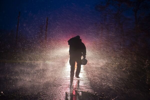 Начальник пожарной службы Монтегута Тоби Генри возвращается к своей пожарной машине под дождем, пока пожарные прорубают деревья на дороге в Бурге, штат Луизиана. - Sputnik Азербайджан