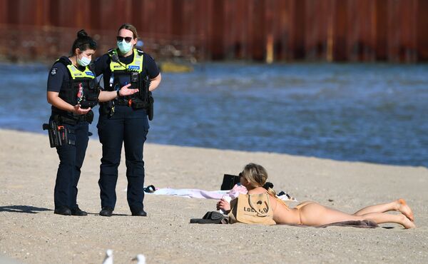 Полиция разговаривает с женщиной, загорающей на пляже Сент-Килда в Мельбурне во время режима самоизоляции. - Sputnik Азербайджан
