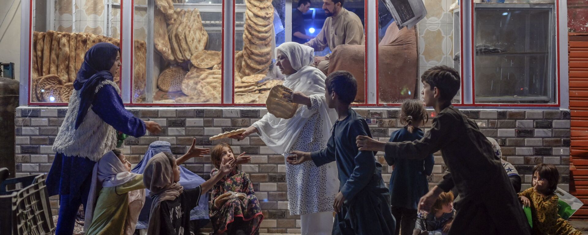 Женщина раздает хлеб нуждающимся детям перед пекарней в Кабуле - Sputnik Азербайджан, 1920, 26.09.2021