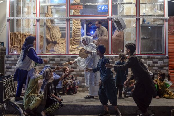 Женщина раздает хлеб нуждающимся детям перед пекарней в Кабуле. - Sputnik Азербайджан
