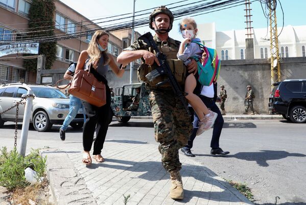 Военнослужащий несет школьника, когда мирные жители бегут из-за перестрелки в Бейруте, Ливан. - Sputnik Азербайджан