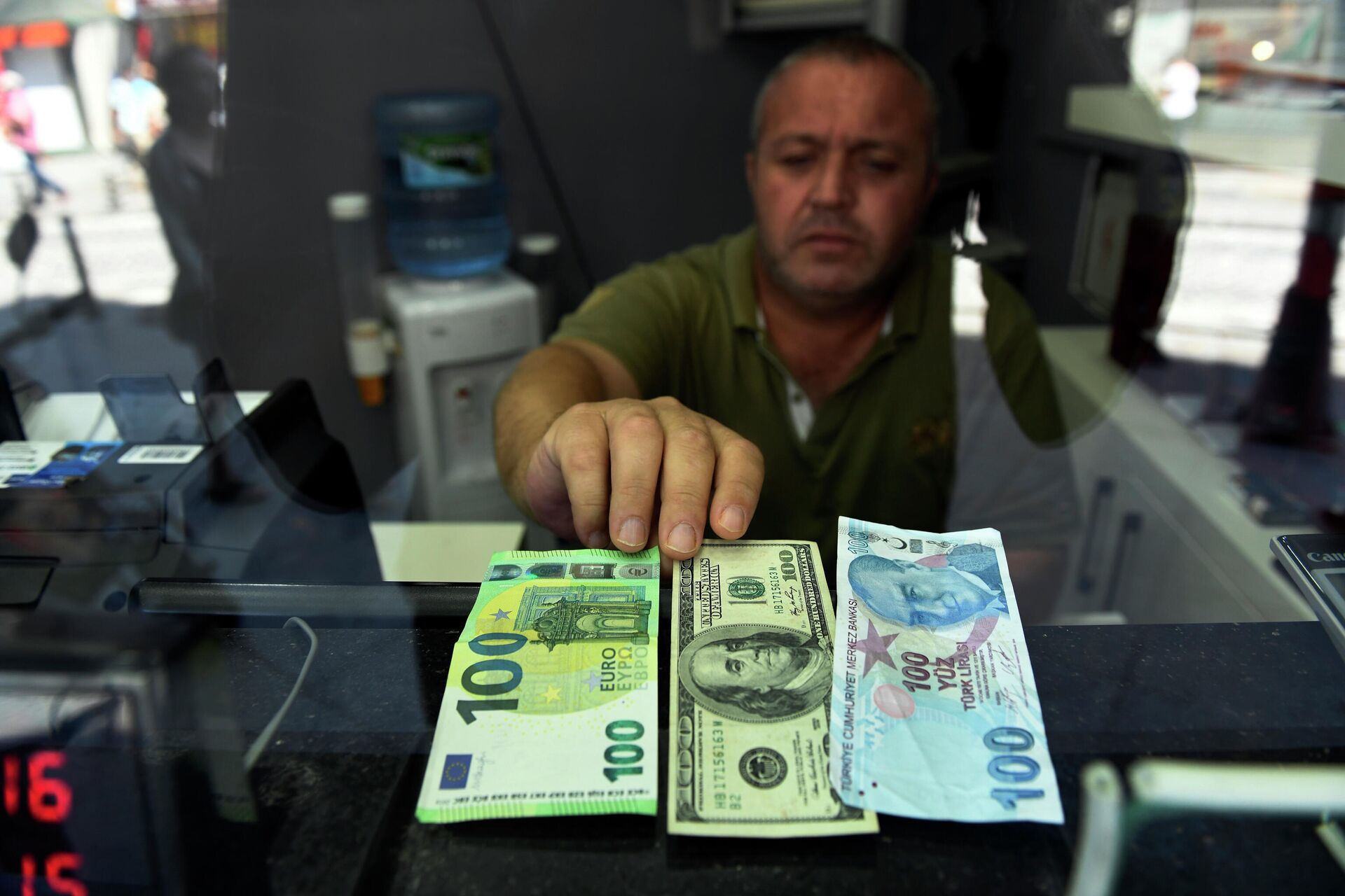 Сотрудник пункта обмена валюты показывает банкноты 100 евро, 100 долларов США и 100 турецких лир, фото из архива - Sputnik Azərbaycan, 1920, 08.06.2024