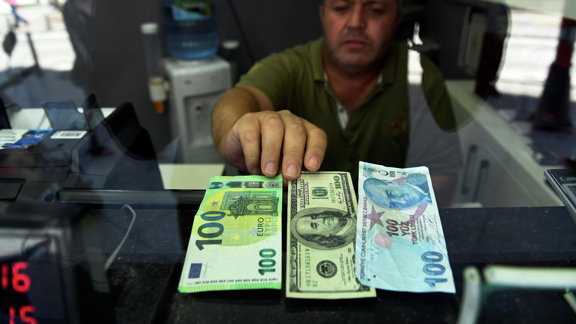 Сотрудник пункта обмена валюты показывает банкноты 100 евро, 100 долларов США и 100 турецких лир, фото из архива - Sputnik Azərbaycan, 1920, 01.12.2021