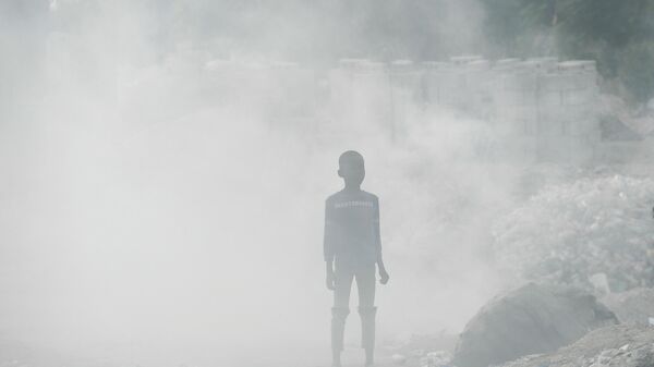 Мальчик стоит посреди дыма от мусора в Порт-о-Пренсе, Гаити. - Sputnik Азербайджан