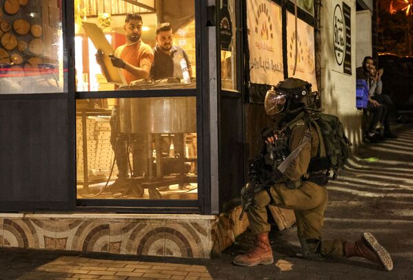 Рабочие в пекарне смотрят на сотрудника израильских сил безопасности во время столкновений с протестующими палестинцами в городе Хеврон. - Sputnik Азербайджан