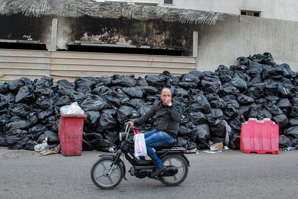 Мужчина зажимает нос, проезжая мимо мешков с мусором, сложенных в центре города Сфакс в Тунисе. - Sputnik Азербайджан