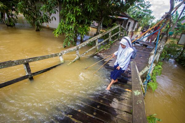 Девушка идет по разрушенному мосту, пострадавшему от разлива реки после наводнения в Индонезии. - Sputnik Азербайджан