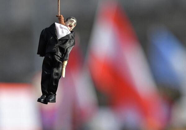 Демонстрант держит макет человека в костюме, висящего на виселице во время митинга в Вене. - Sputnik Азербайджан