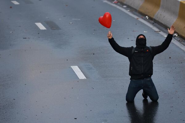 Протестующий с воздушным шаром в форме сердца стоит на коленях на улице в Брюсселе. - Sputnik Азербайджан