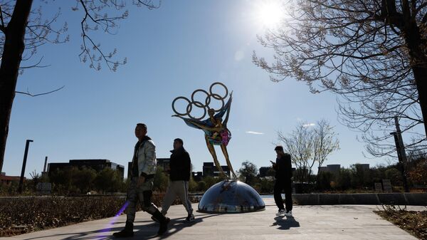 Люди проходя мимо скульптуры в виде олимпийских колец в Пекине - Sputnik Азербайджан
