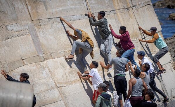 Мигранты взбираются на стену в северном городе Фнидек на испано-марокканской границе у Сеуты, 19 мая 2021 года. - Sputnik Азербайджан