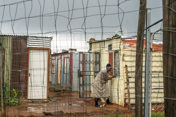 Женщина закрывает окна своего дома на территории неформального поселения в окрестностях Йоханнесбурга, ЮАР. - Sputnik Азербайджан