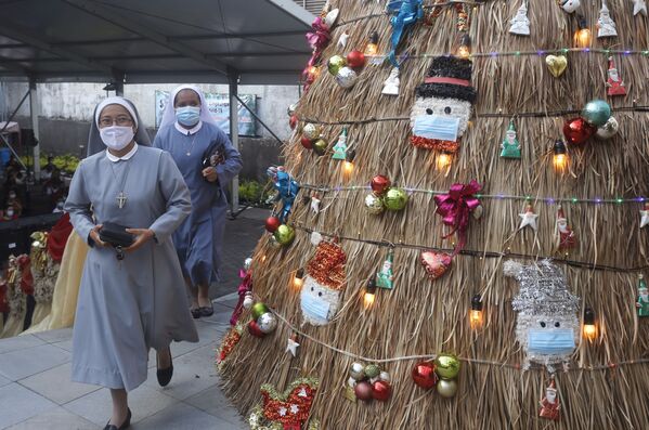 Монахини проходят мимо рождественской елки с украшением на тему коронавируса перед рождественской службой в церкви на Бали, Индонезия. - Sputnik Азербайджан