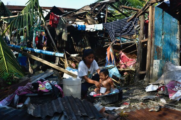 Жительница купает своего ребенка рядом с разрушенным домом в Каркаре, Филиппины. - Sputnik Азербайджан