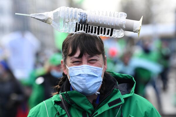 Медицинский работник с символическим предметом в форме шприца на голове во время протестов против обязательной вакцинации против Covid-19 в Бельгии, 7 декабря 2021 года - Sputnik Азербайджан