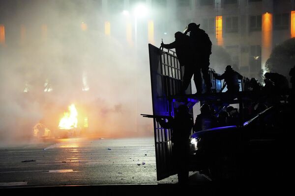 Полицейская машина горит, когда ОМОН готовится остановить протестующих в центре Алматы. - Sputnik Азербайджан