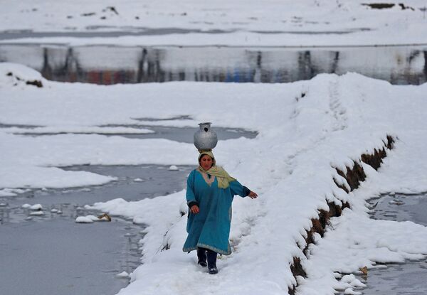 Женщина несёт воду в кувшине на голове по заснеженному полю на окраине индийского города Сринагар. - Sputnik Азербайджан
