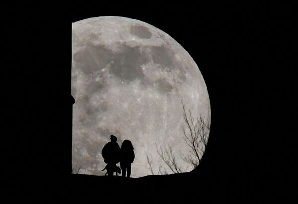 Люди выгуливают собаку на вершине холма Гластонбери-Тор, когда восходит &quot;Волчья луна&quot;, Великобритания. - Sputnik Азербайджан