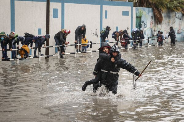 Муниципальный работник переносит школьника на другой край улицы во время ливневых затоплений в Газе. - Sputnik Азербайджан