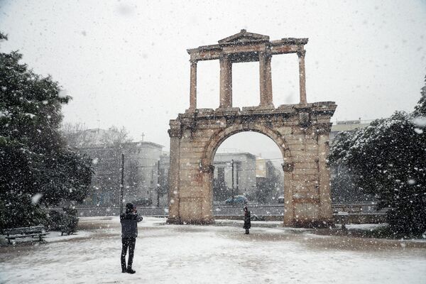 Люди наслаждаются снегом у ворот Адриана во время сильного снегопада в Афинах, Греция. - Sputnik Азербайджан