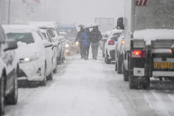 Люди идут посреди улицы во время снегопада в Агиос-Стефанос, к северу от Афин. По прогнозам синоптиков, снегопад в Греции продолжится до 25 января. - Sputnik Азербайджан