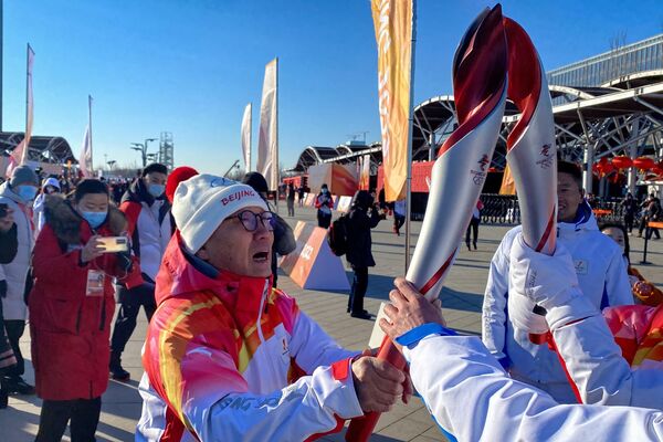 Ло Чжихуань (слева), первая чемпионка мира по конькобежному спорту из Китая, проходит мимо олимпийского огня. - Sputnik Азербайджан