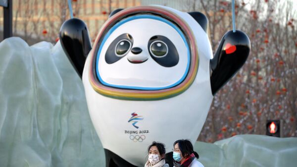 Люди в масках для защиты от коронавируса проходят мимо талисмана Зимних Олимпийских игр Бин Дуньдуня возле Олимпийского поля в Пекине - Sputnik Азербайджан