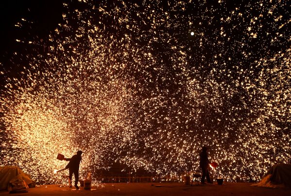 Кузнецы создают дождь искр из расплавленного метала накануне Фестиваля фонарей в пекинском парке. - Sputnik Азербайджан