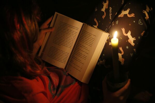 Ребенок читает книгу при свечах во время тестового отключения электричества в Киеве - Sputnik Азербайджан