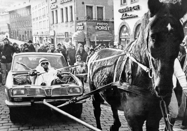 Улицы в Германии изменились до неузнаваемости. Вот, например, мужчина в костюме шейха держит поводья лошади, которая тащит автомобиль, переделанный в повозку. Нюрнберг,  25 ноября 1973. - Sputnik Азербайджан