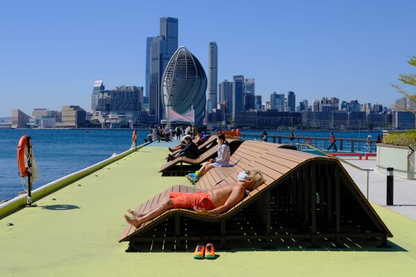 Мужчина в маске наслаждается солнечными ваннами в прибрежном парке Гонконга. - Sputnik Азербайджан